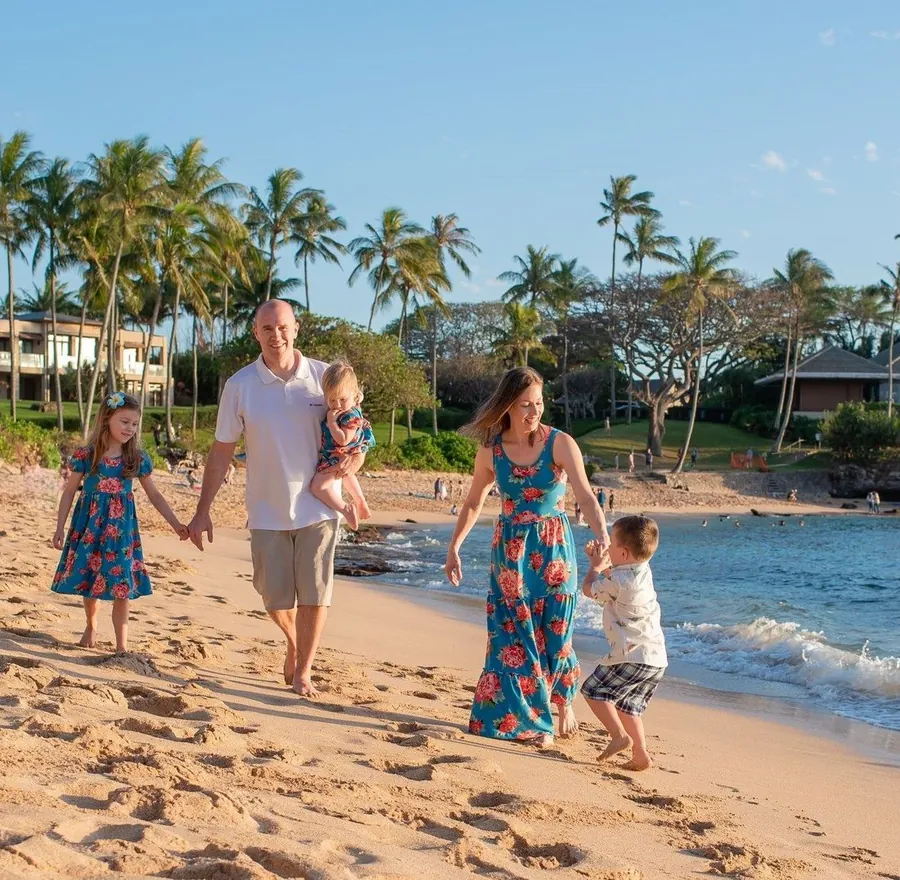 A family walking hand in hand along a palm-lined Hawaiian beach at golden hour